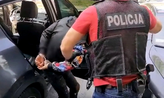 policjant z zatrzymanym mężczyzną zakutym w kajdanki przy radiowozie policyjnym