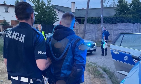 Policjant prowadzi do radiowozu zatrzymanego motocyklistę