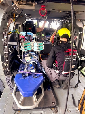 wnętrze śmigłowca, nosze, aparatura medyczna do monitorowania stanu pacjenta, obok noszy ratownik LPR, w głębi policyjny lotnicy w fotelach