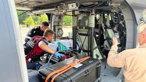 dwaj ratownicy przy noszach z pacjentem w śmigłowcu stojącym na lądowisku