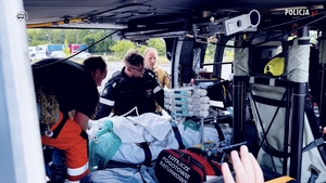 Pacjent na noszach we wnętrzu śmigłowca stojącego na lotnisku. Obok niego ratownicy i aparatura medyczna.