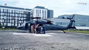 Ratownicy i piloci z pacjentem na noszach przy śmigłowcu stojącym na lądowisku przy szpitalu.