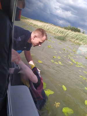 policjant na łodzi policyjnej wyciąga z wody mężczyznę