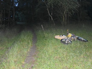 przewrócony na drodze motocykl leżący na skraju polnej drogi w tle drzewa