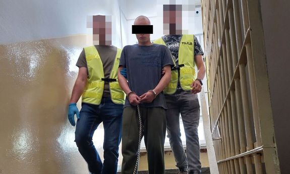 Dwaj policjanci w żółtych kamizelkach prowadzą zatrzymanego mężczyznę