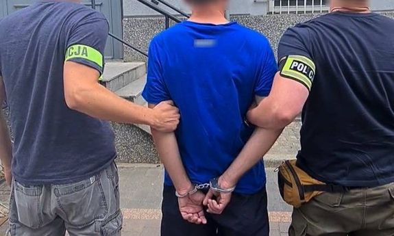 dwaj ubrani po cywilnemu policjanci, z opaskami na rękach z napisem Policja, prowadzą zatrzymanego - widok z tyłu