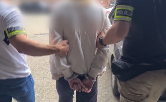 dwaj ubrani po cywilnemu policjanci prowadzą zatrzymana kobietę w kajdankach