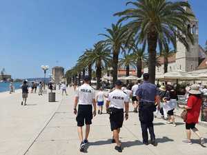 Nabrzeże portowe, z lewej zatoka, z prawej palmy, na pierwszym planie odwróceni tyłem trzej umundurowani policjanci z tego dwaj w białych koszulkach z napisem Policja. Trzeci w koszuli w kolorze niebieskim.