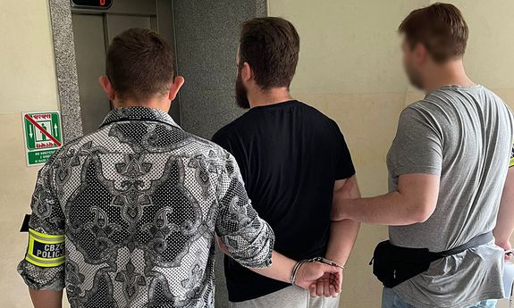dwaj nieumundurowani policjanci prowadzą zatrzymanego mężczyznę