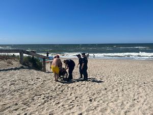 Troje policjantów pomaga mężczyźnie na wózku inwalidzkim wydostać się z plaży