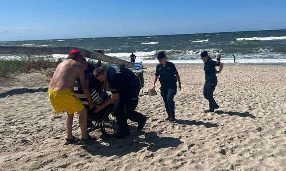 Troje policjantów pomaga mężczyźnie na wózku inwalidzkim wydostać się z plaży
