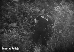 Czarno - białe zdjęcie przedstawiające policjanta, podczas poszukiwań wśród krzewów