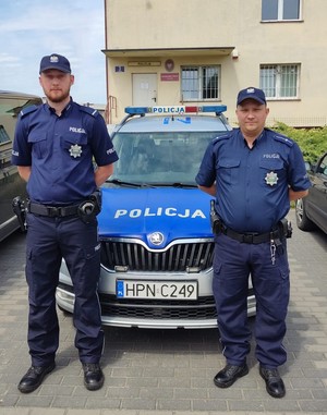 dwaj policjanci stoją przed radiowozem policyjnym zaparkowanym przed budynkiem Posterunku Policji w Zblewie