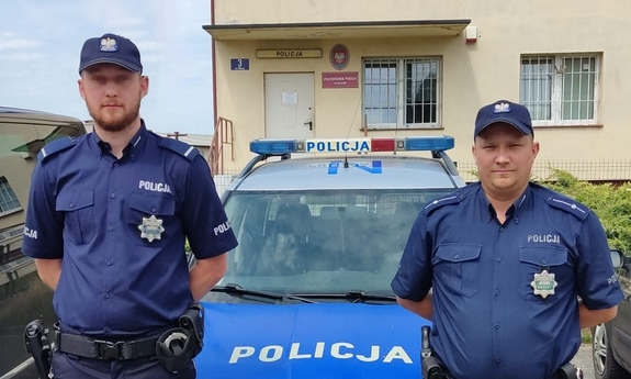 dwaj policjanci stoją przed radiowozem policyjnym zaparkowanym przed budynkiem Posterunku Policji w Zblewie