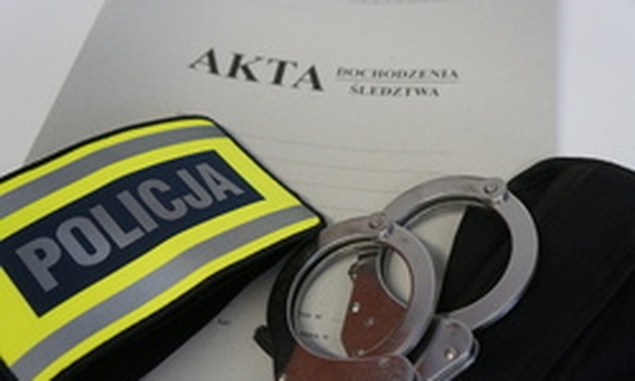 na teczce z aktami sprawy leżą kajdanki i opaska naramienna z napisem policja