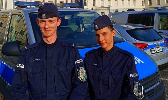 Policjant i policjantka, w tle radiowozy policyjne