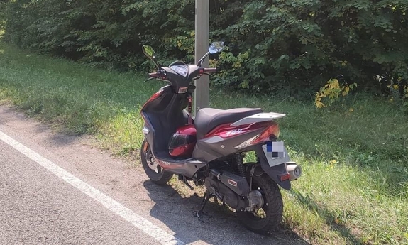 Motorower stojący na poboczu drogi, Wzdłuż drogi gęsto rosną drzewa.