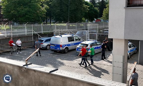 policjanci prowadzą zatrzymanego, wokół widać zaparkowane radiowozy