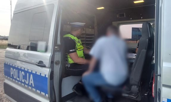 w policyjnym furgonie siedzi policjant ruchu drogowego a przed im mężczyzna