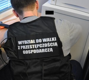 policjant w kamizelce z napisem Przestępczość gospodarcza w trakcie otwierania metalowej szafy
