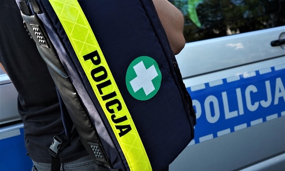 policjant trzymający torbę ze sprzętem medycznym. Torba z napisem policja, w tle radiowóz