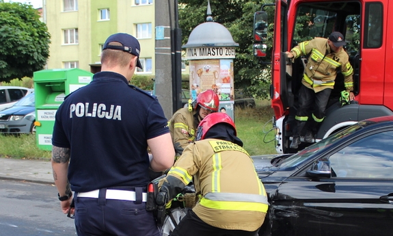 policjant stoi przy samochodzie poszkodowanego mężczyzny i strażacy pracujący przy samochodzie