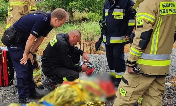 Mężczyzna leżący na noszach w obecności policjanta i strażaków