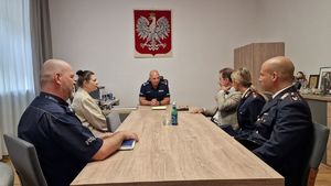 Czworo umundurowanych policjantów, dwóch polskich policjantów, dwoje włoskich policjantów oraz dwie osoby w ubraniu cywilnym siedzące przy stole w gabinecie z godłem.