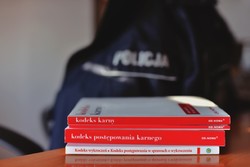Na zdjęciu leżący na stole Kodeks karny, Kodeks postępowania karnego oraz Kodeks wykroczeń. W tle mundur policyjny