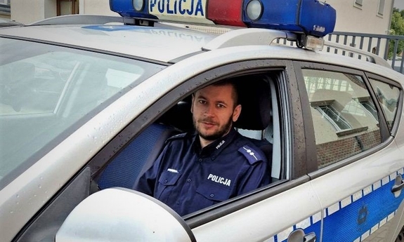 policjant siedzi za kierownica radiowozu policyjnego