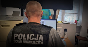 policjant siedzi przed komputerem, na plecach ma napis: Policja, technik kryminalistyki