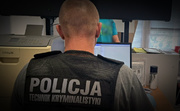 policjant siedzi przed komputerem, na plecach ma napis: Policja, technik kryminalistyki