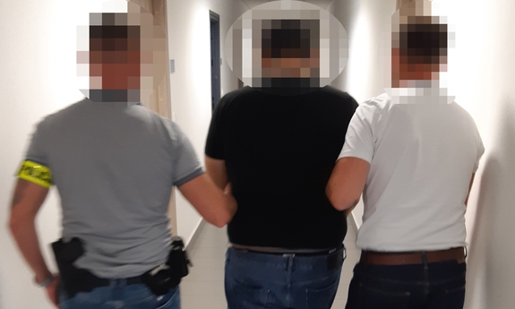 Dwaj nieumundurowani policjanci prowadzą korytarzem zatrzymanego mężczyznę