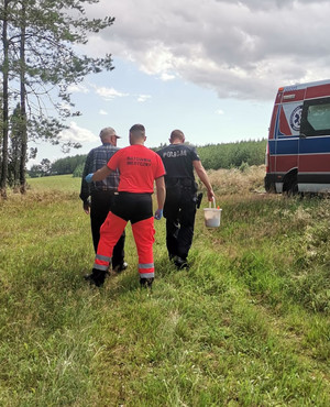 policjant i ratownik medyczny wyprowadzają z lasu odnalezionego mężczyznę