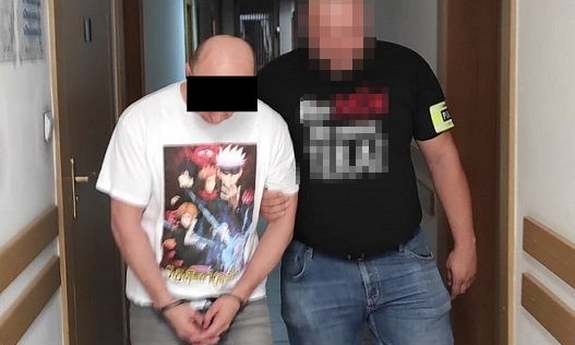 policjant prowadzi zatrzymaną osobę zakutą w kajdanki