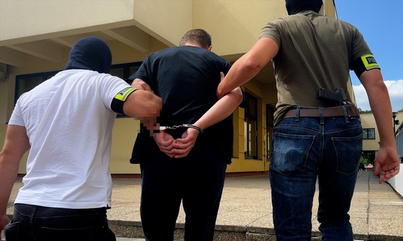 dwaj nieumundurowani policjanci prowadza zatrzymanego zakutego w kajdanki