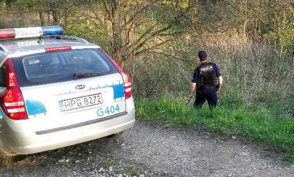 na drodze gruntowej stoi radiowóz, obok policjant na tle lasu