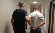 policjant z zatrzymanym zakutym w kajdanki na korytarzu w budynku komendy Policji