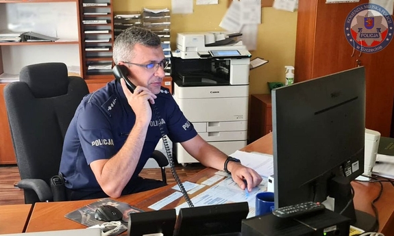 policjant dyżurny siedzi przy biurku rozmawiając przez telefon