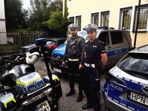 dwaj policjanci stoją na policyjnym parkingu obok motocykla i radiowozów