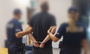 Policjant i policjantka z zatrzymanym mężczyzną zakutym w kajdanki widziani od tyłu