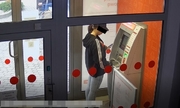 kobieta w czapce z daszkiem trzyma telefon w ręku i stoi naprzeciwko bankomatu