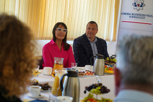 Kobieta i mężczyzna siedzący przy stoliku, za nimi roll-up Komendy Wojewódzkiej w Bydgoszczy