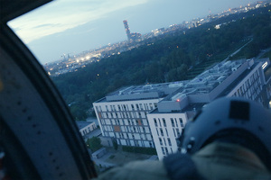 Członek załogi policyjnego śmigłowca obserwuje widoczny w dole budynek szpitala.