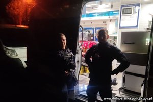 Policjantka i policjant stojący nocną porą przy ambulansie