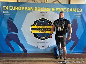 Dobrze zbudowany mężczyzna w stroju sportowym stojący przy banerze z napisami po angielsku 9 European Police Fire Games