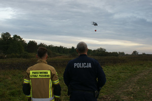 Policjant i strażak obserwują lecący śmigłowiec.
