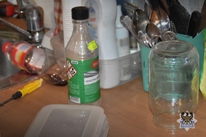 Butelka z benzyną ekstrakcyjną znajdujący się koło zlewu w kuchni koło naczyń i innego sprzętu kuchennego