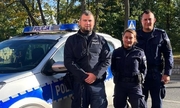 dwaj policjanci i policjantka stoją przy radiowozie policyjnym