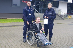 policjanci przy młodym mężczyźnie siedzącym na wózku inwalidzkim, w tle wejście do komendy